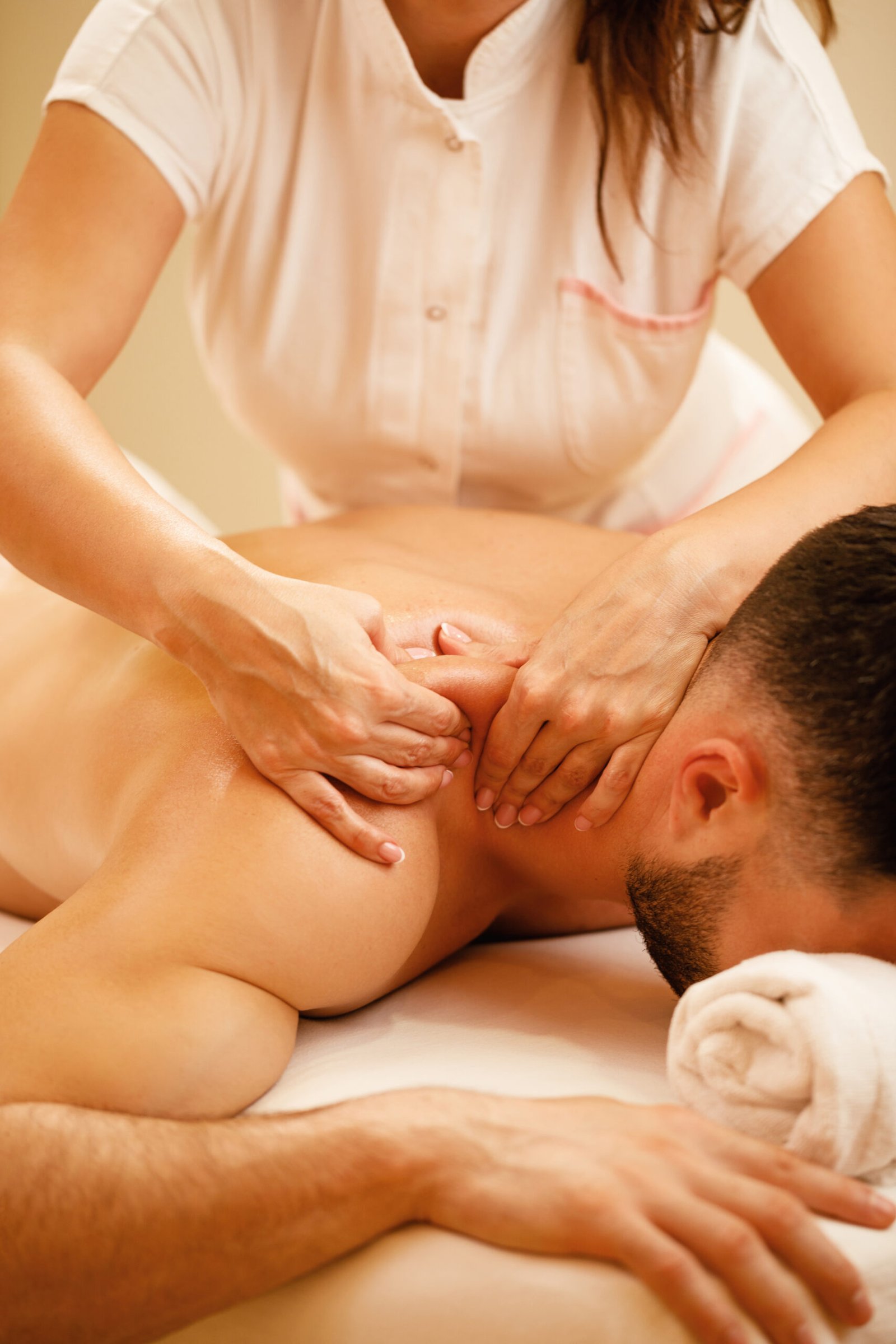 unrecognizable therapist massaging man's shoulders during spa treatment.